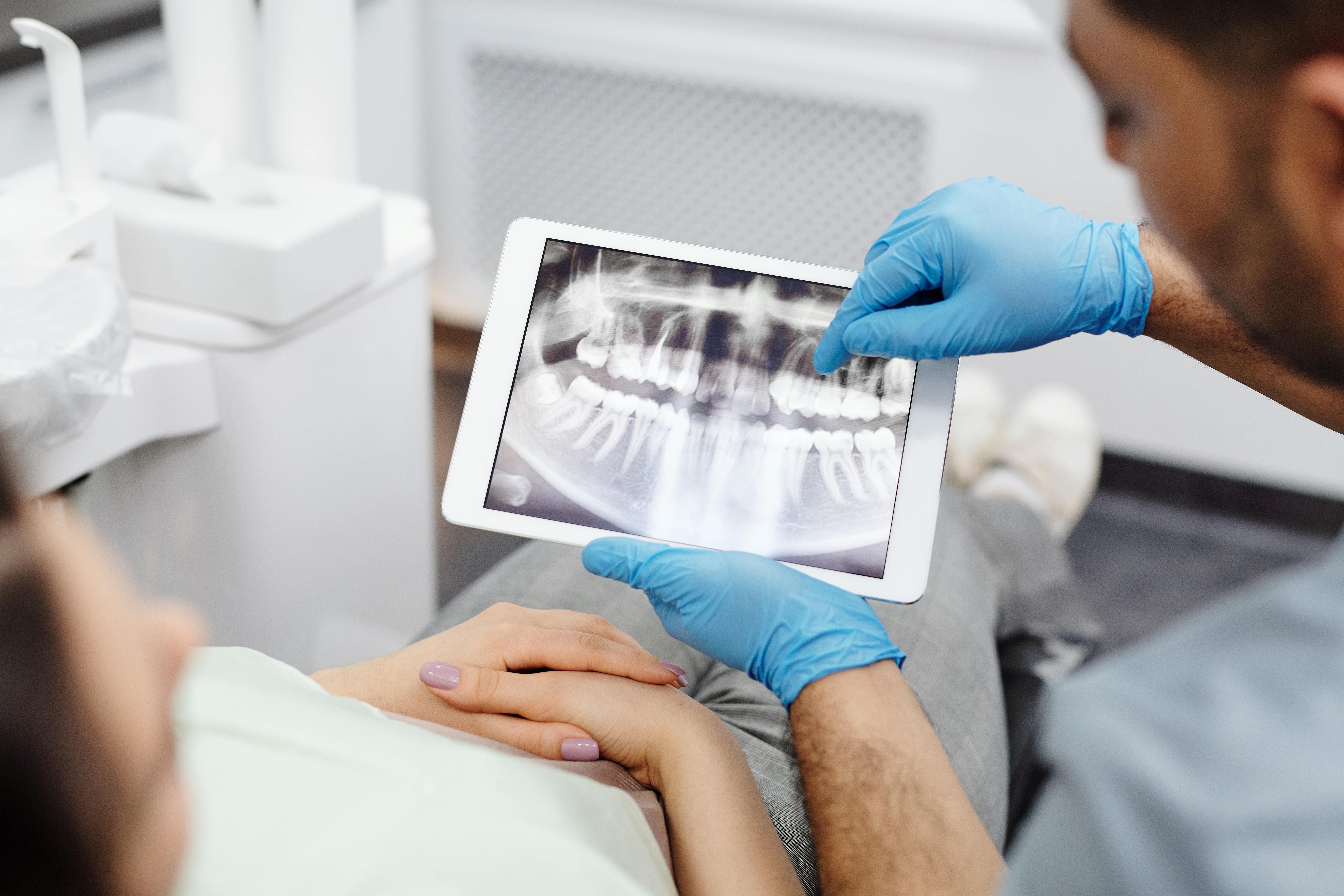 diş hekimi tabletten hastasının diş röntgenini ve problemleri gösteriyor