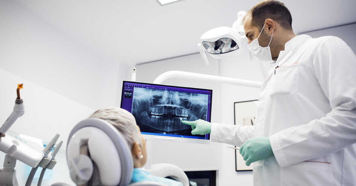 A dentist showing a patient the details of their panoramic teeth x-ray image.