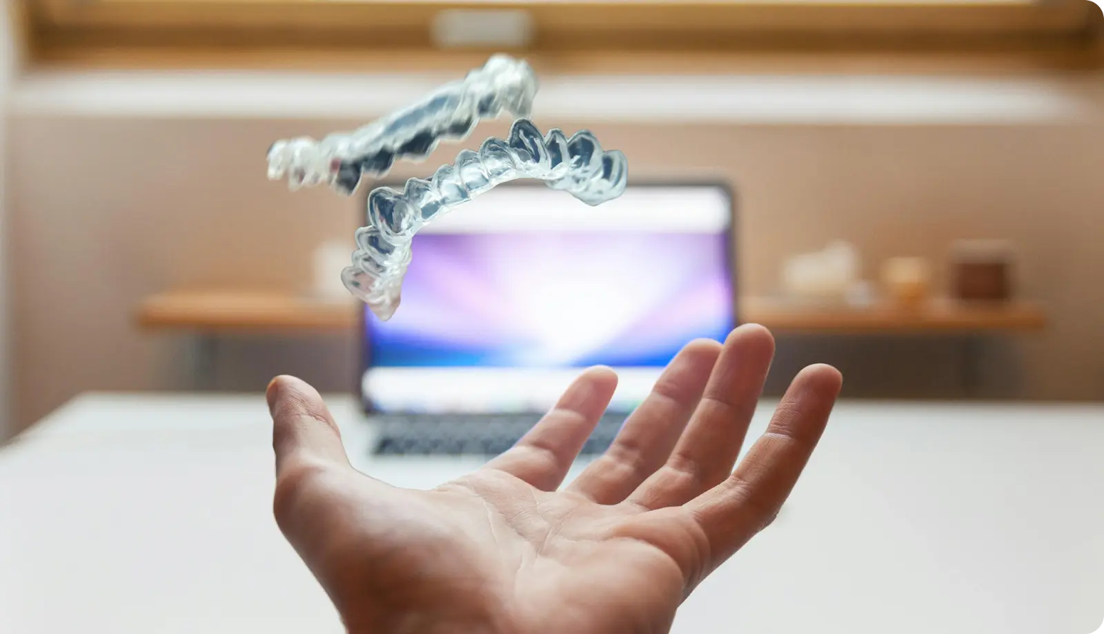 Conceptual visualization of digital dentistry showing invisible aligners floating above a laptop, representing future dental technologies.