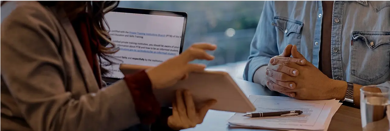 Two people discussing documents over a tablet and a laptop at a meeting table
