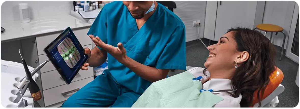 Dentist showing AI-marked radiograph findings on a tablet to a smiling patient in the chair