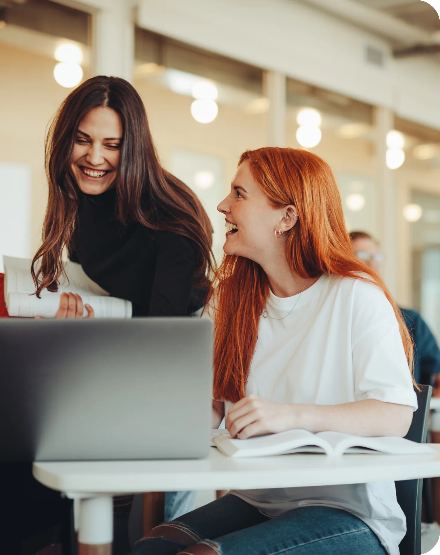 Two colleagues talking and smiling at a sunlit table next to a laptop